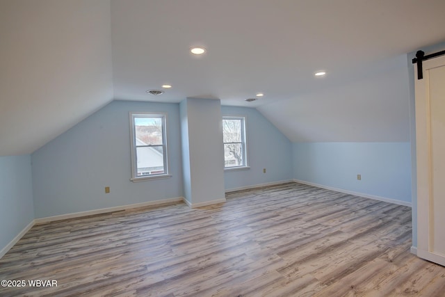 bonus room featuring visible vents, light wood-style floors, a barn door, and vaulted ceiling