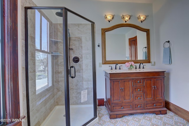 bathroom with a stall shower, double vanity, a sink, and baseboards