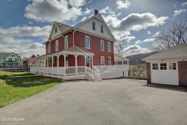 victorian-style house with a front yard, brick siding, a chimney, and covered porch