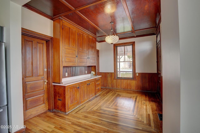 kitchen with parquet floors, light countertops, wainscoting, hanging light fixtures, and brown cabinets