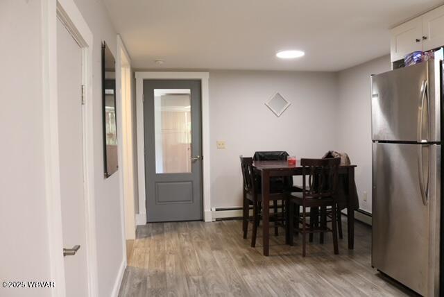 dining room with a baseboard heating unit, light wood-style flooring, and baseboards