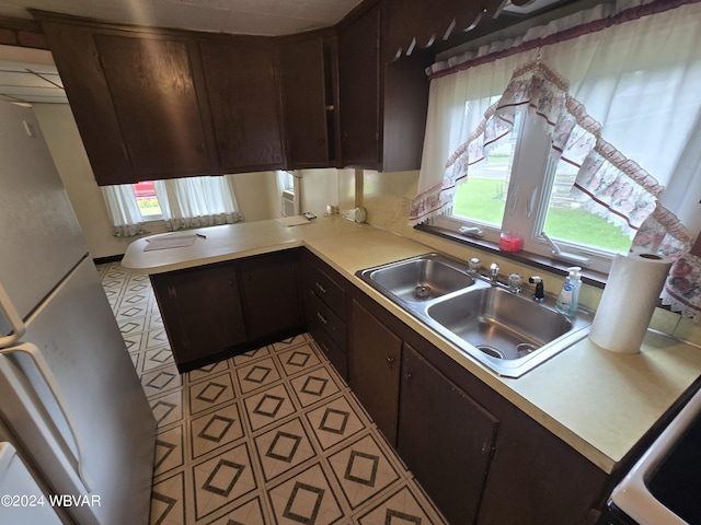 kitchen featuring light tile patterned flooring, dark brown cabinetry, white fridge, and sink