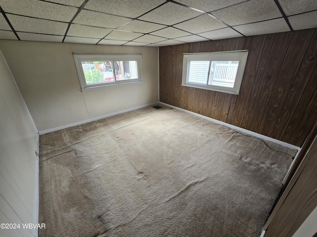 carpeted spare room featuring a drop ceiling and wood walls