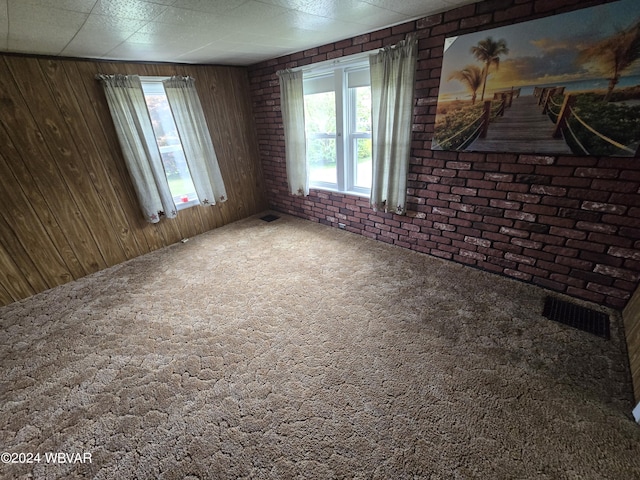 carpeted spare room with wood walls and brick wall