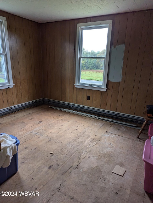 empty room featuring baseboard heating, wooden walls, and light hardwood / wood-style flooring