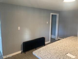 kitchen with wood finished floors, radiator heating unit, a baseboard radiator, baseboards, and light stone countertops