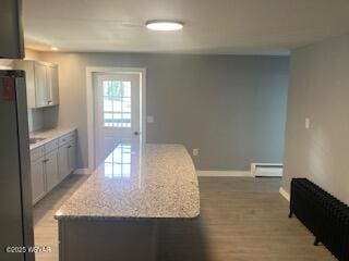 kitchen with light wood-type flooring, a center island, freestanding refrigerator, a baseboard radiator, and baseboards