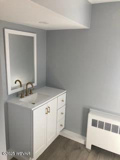 bathroom featuring baseboards, radiator, wood finished floors, and vanity