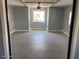 spare room with crown molding, baseboards, beam ceiling, wood finished floors, and a baseboard radiator