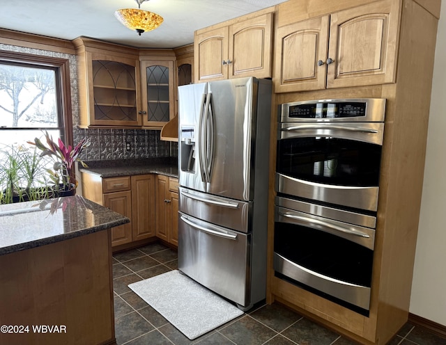 kitchen with appliances with stainless steel finishes, backsplash, dark tile patterned floors, and dark stone countertops