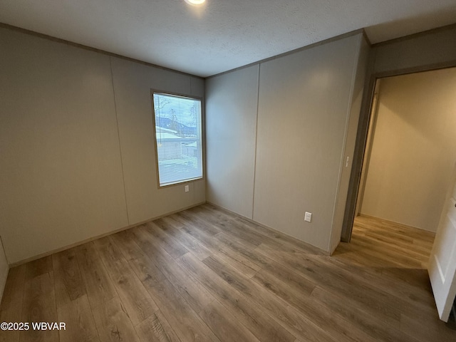 empty room with a textured ceiling and light hardwood / wood-style flooring