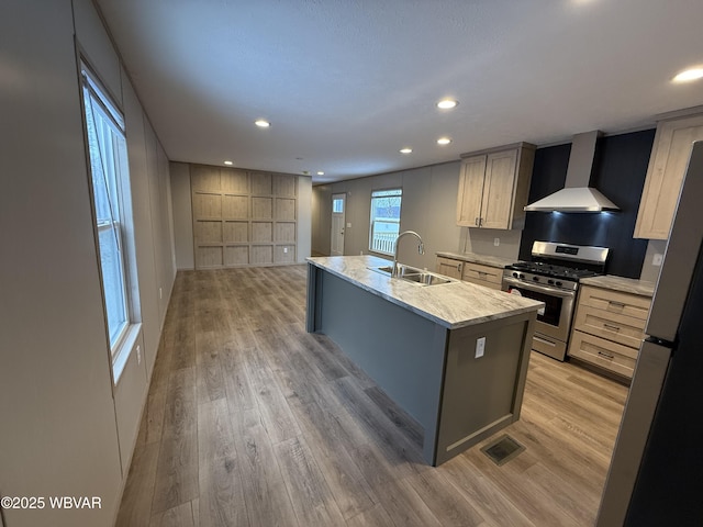 kitchen with gas range, sink, wall chimney exhaust hood, fridge, and a center island with sink