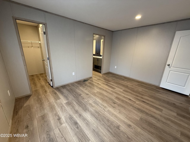 unfurnished bedroom featuring a walk in closet, light hardwood / wood-style floors, ensuite bath, and a closet