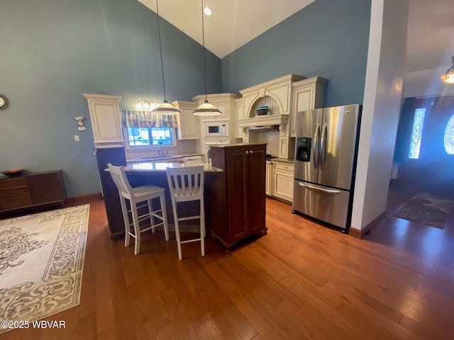 kitchen with pendant lighting, stainless steel refrigerator with ice dispenser, white microwave, dark hardwood / wood-style floors, and high vaulted ceiling