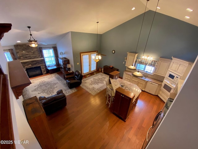 living room featuring ceiling fan, french doors, a stone fireplace, hardwood / wood-style floors, and high vaulted ceiling