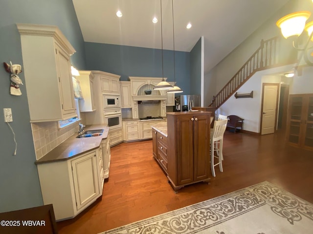 kitchen with hardwood / wood-style floors, appliances with stainless steel finishes, an island with sink, decorative backsplash, and hanging light fixtures