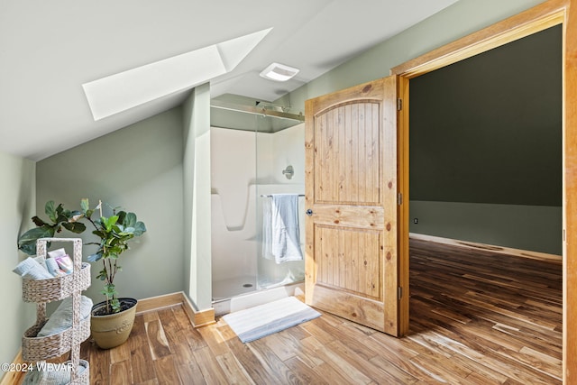 full bath featuring a stall shower, baseboards, lofted ceiling with skylight, and wood finished floors