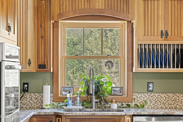 kitchen with appliances with stainless steel finishes, a sink, light stone counters, and tasteful backsplash