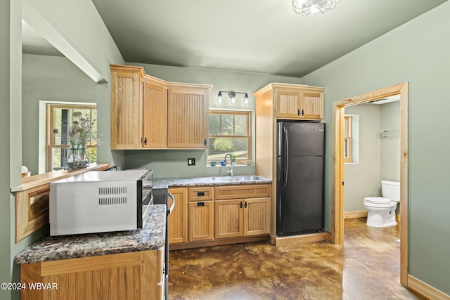 kitchen featuring light brown cabinetry, freestanding refrigerator, a sink, concrete flooring, and baseboards