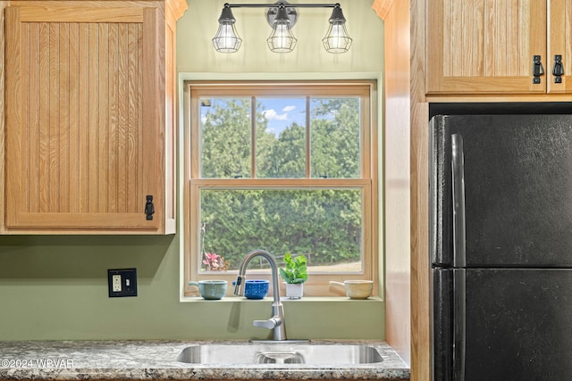 kitchen featuring freestanding refrigerator, light stone countertops, a sink, and light brown cabinetry