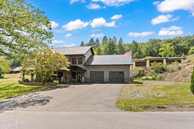 view of front of home featuring a garage, driveway, stone siding, metal roof, and a standing seam roof