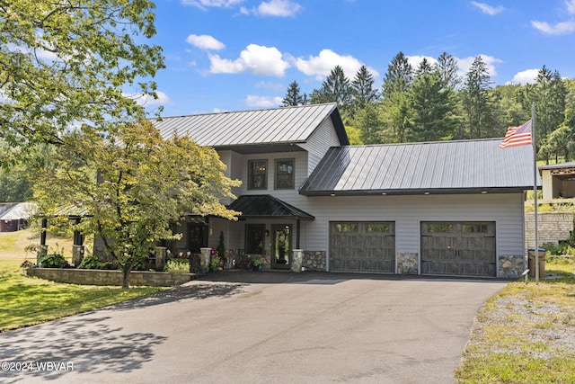 view of front of property featuring metal roof, aphalt driveway, an attached garage, stone siding, and a standing seam roof