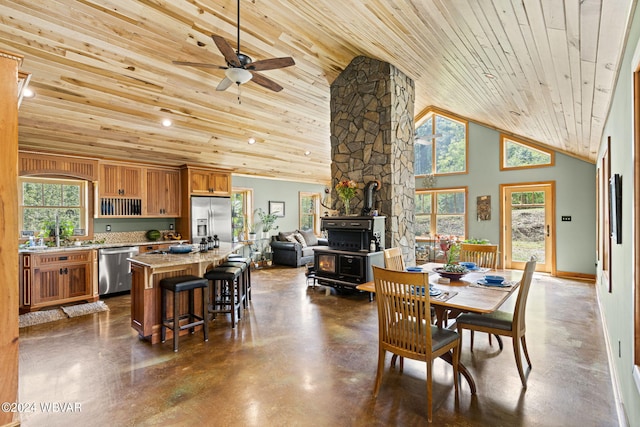 dining space featuring high vaulted ceiling, a wood stove, a healthy amount of sunlight, and concrete flooring