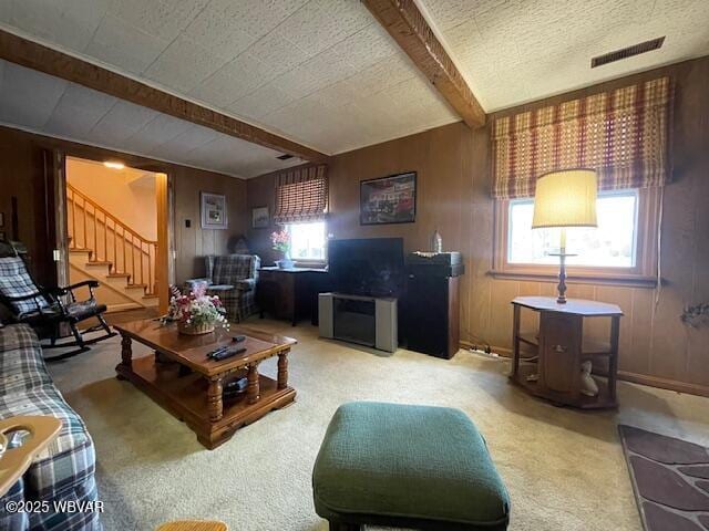 carpeted living room featuring beam ceiling, a textured ceiling, and wooden walls