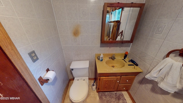 bathroom featuring toilet, tile patterned floors, vanity, and tile walls