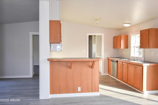 kitchen with kitchen peninsula, light wood-type flooring, sink, dishwasher, and lofted ceiling