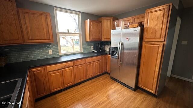 kitchen with light wood-type flooring, dark countertops, brown cabinets, and stainless steel refrigerator with ice dispenser