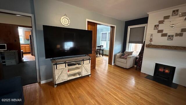 living area with light wood finished floors, a fireplace with flush hearth, and baseboards