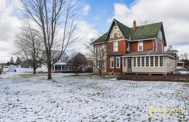 snow covered back of property with a sunroom