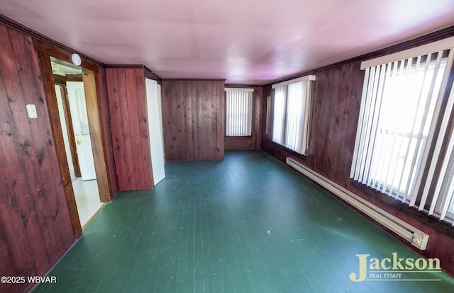 spare room with crown molding, a healthy amount of sunlight, wooden walls, and a baseboard radiator