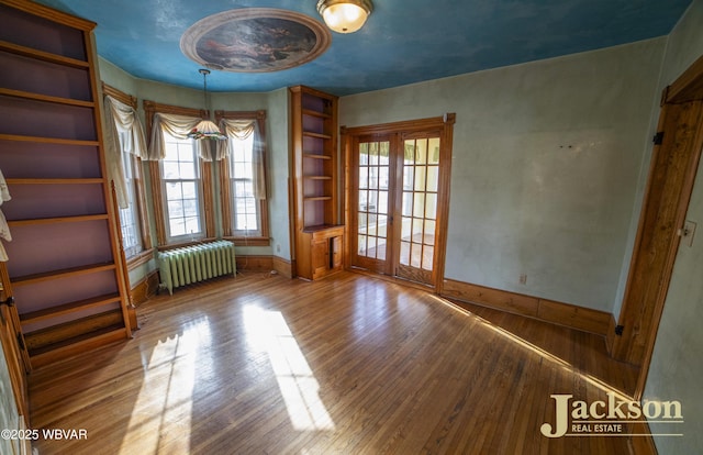 empty room featuring hardwood / wood-style floors, radiator heating unit, and french doors