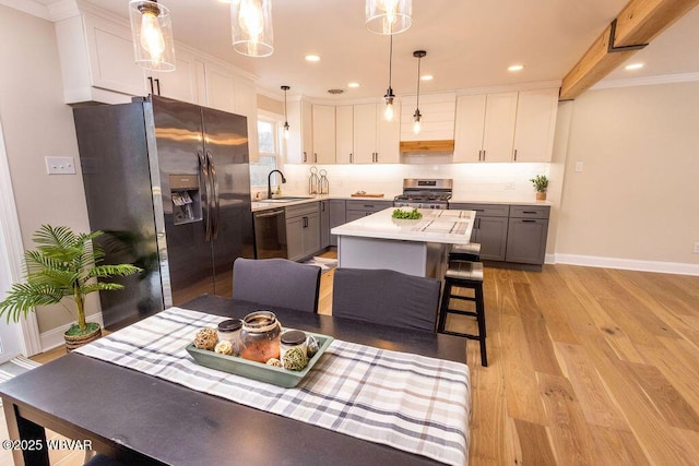 kitchen featuring gray cabinetry, a kitchen island, light countertops, appliances with stainless steel finishes, and decorative light fixtures