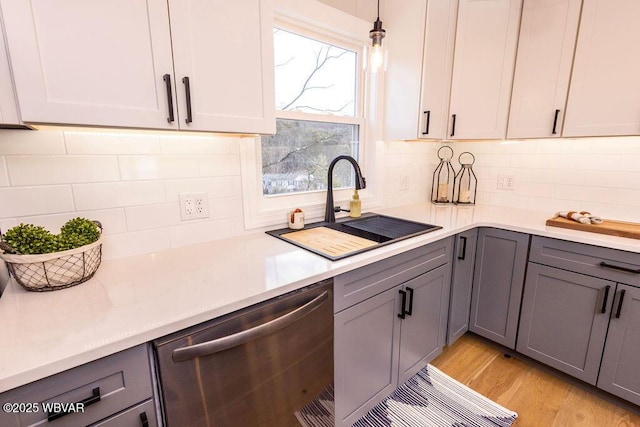 kitchen with decorative light fixtures, light countertops, gray cabinetry, stainless steel dishwasher, and a sink