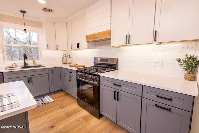 kitchen featuring gray cabinets, light countertops, white cabinetry, a sink, and stainless steel gas range