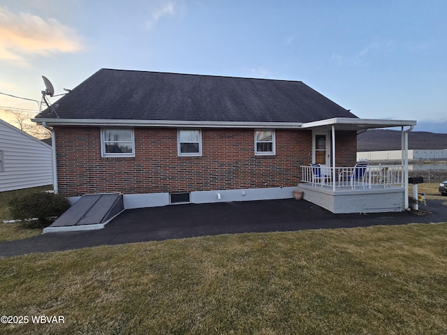 rear view of property featuring a porch, brick siding, roof with shingles, and a lawn