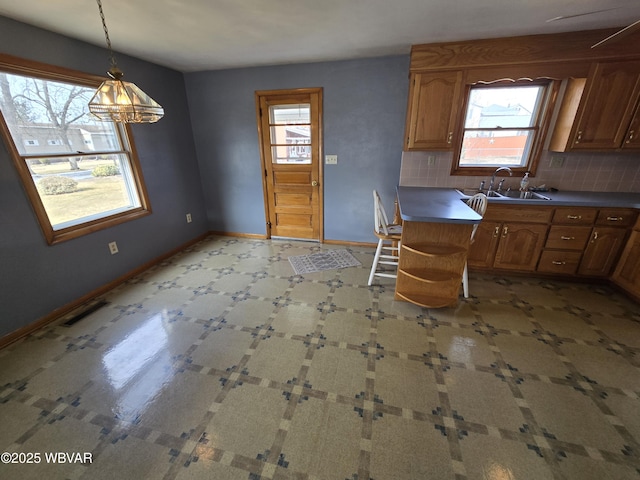 kitchen with visible vents, baseboards, a sink, hanging light fixtures, and backsplash