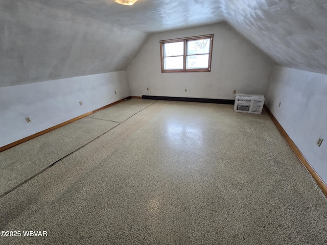 additional living space with vaulted ceiling, baseboards, and a textured ceiling