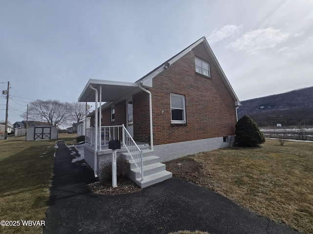 view of home's exterior featuring an outbuilding, a shed, a porch, a yard, and brick siding