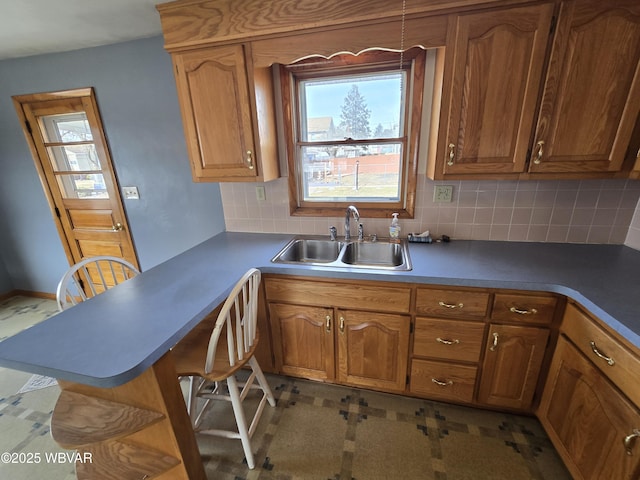 kitchen featuring tasteful backsplash, brown cabinets, a peninsula, and a sink