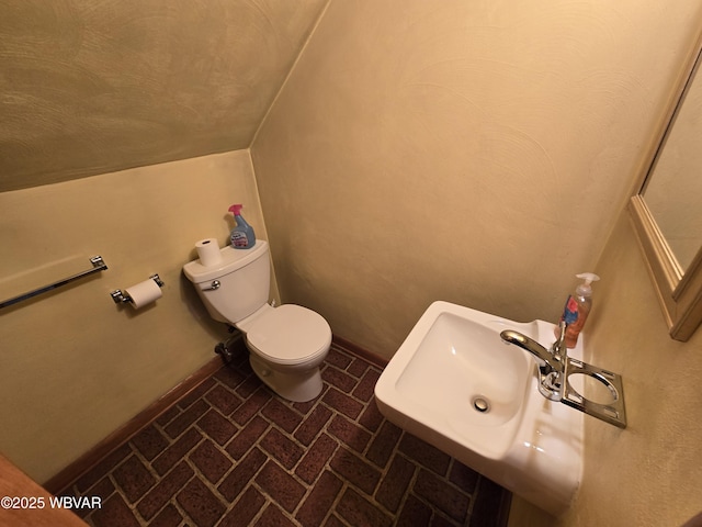 half bath featuring toilet, brick floor, and baseboards