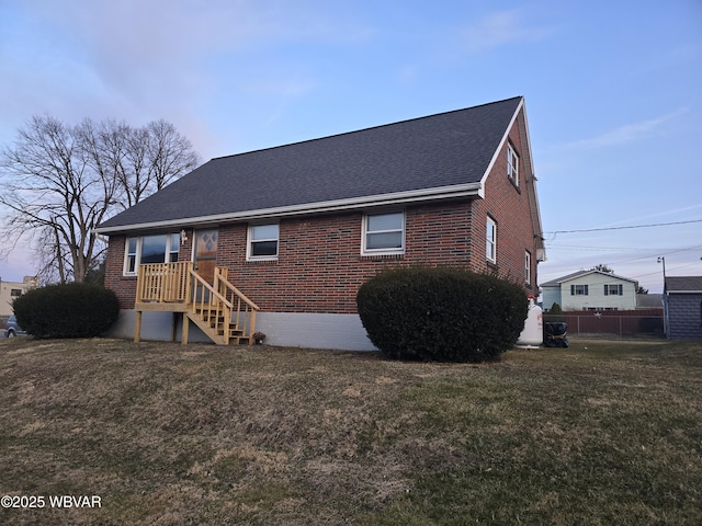 view of front facade featuring brick siding, roof with shingles, a front lawn, and fence