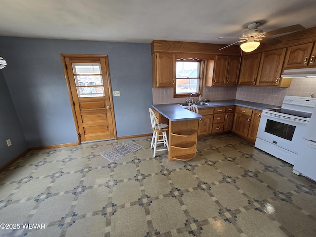 kitchen featuring baseboards, electric stove, under cabinet range hood, brown cabinets, and backsplash