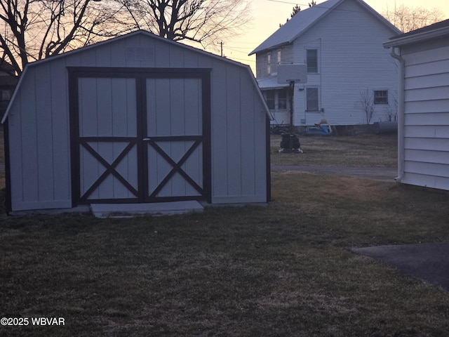 outdoor structure at dusk featuring a storage shed, a yard, and an outbuilding