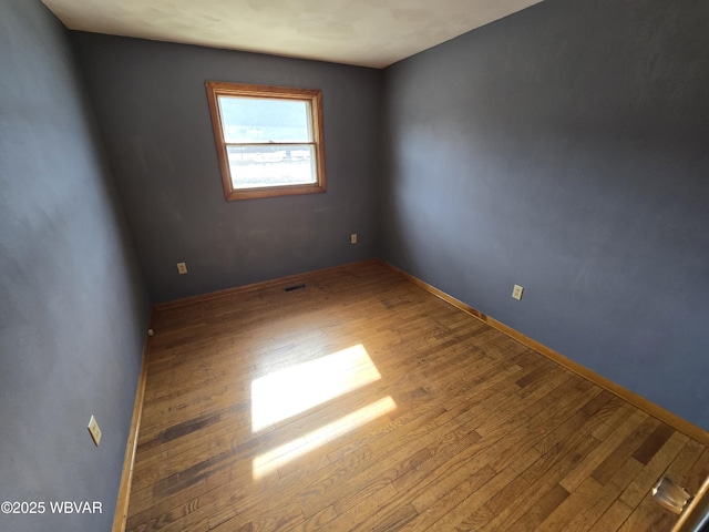 unfurnished room with visible vents, baseboards, and hardwood / wood-style flooring