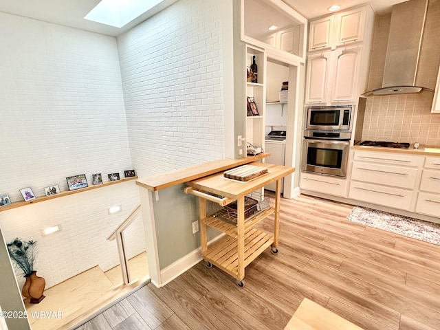 2035 Woodland Rd, Montoursville, PA 17754 - kitchen with stainless steel appliances, a skylight, wall chimney exhaust hood, light wood-type flooring, and tasteful backsplash