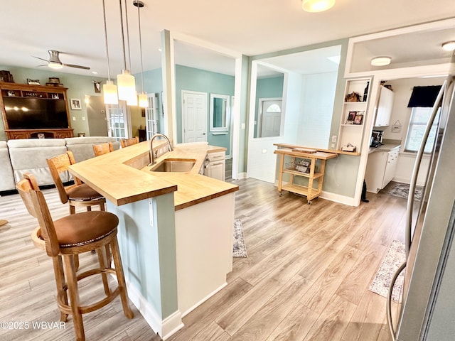 2035 Woodland Rd, Montoursville, PA 17754 - kitchen with butcher block countertops, a sink, ceiling fan, a kitchen bar, and light wood finished floors
